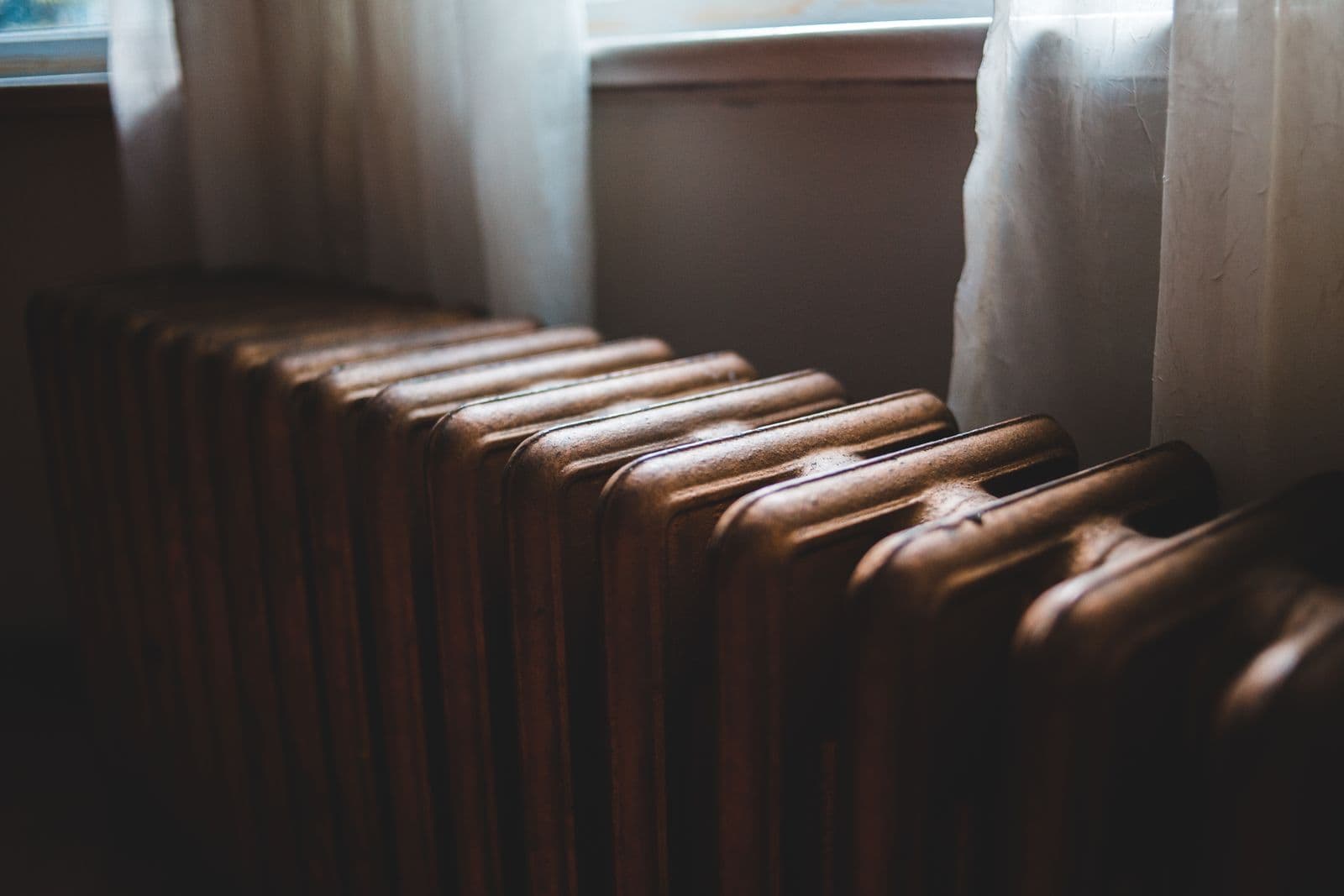Radiateur en fonte près d'une fenêtre à rideaux, lumière douce d'un intérieur bruxellois